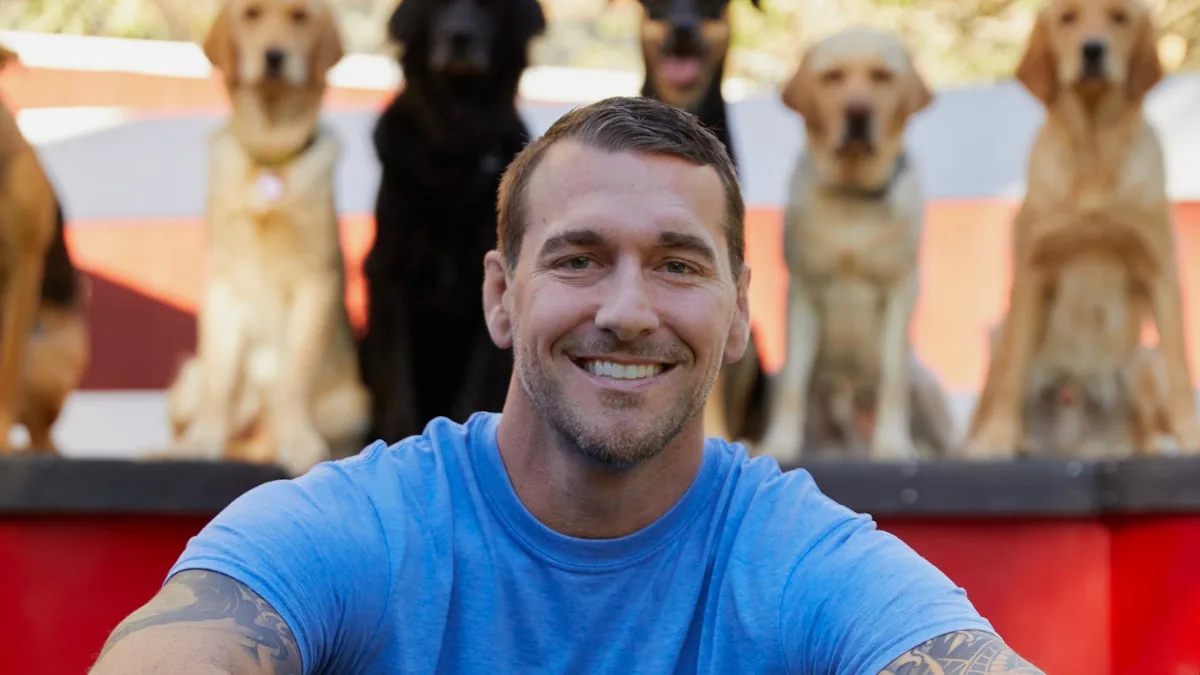Brandon McMillan smiling with a row of retrievers behind him