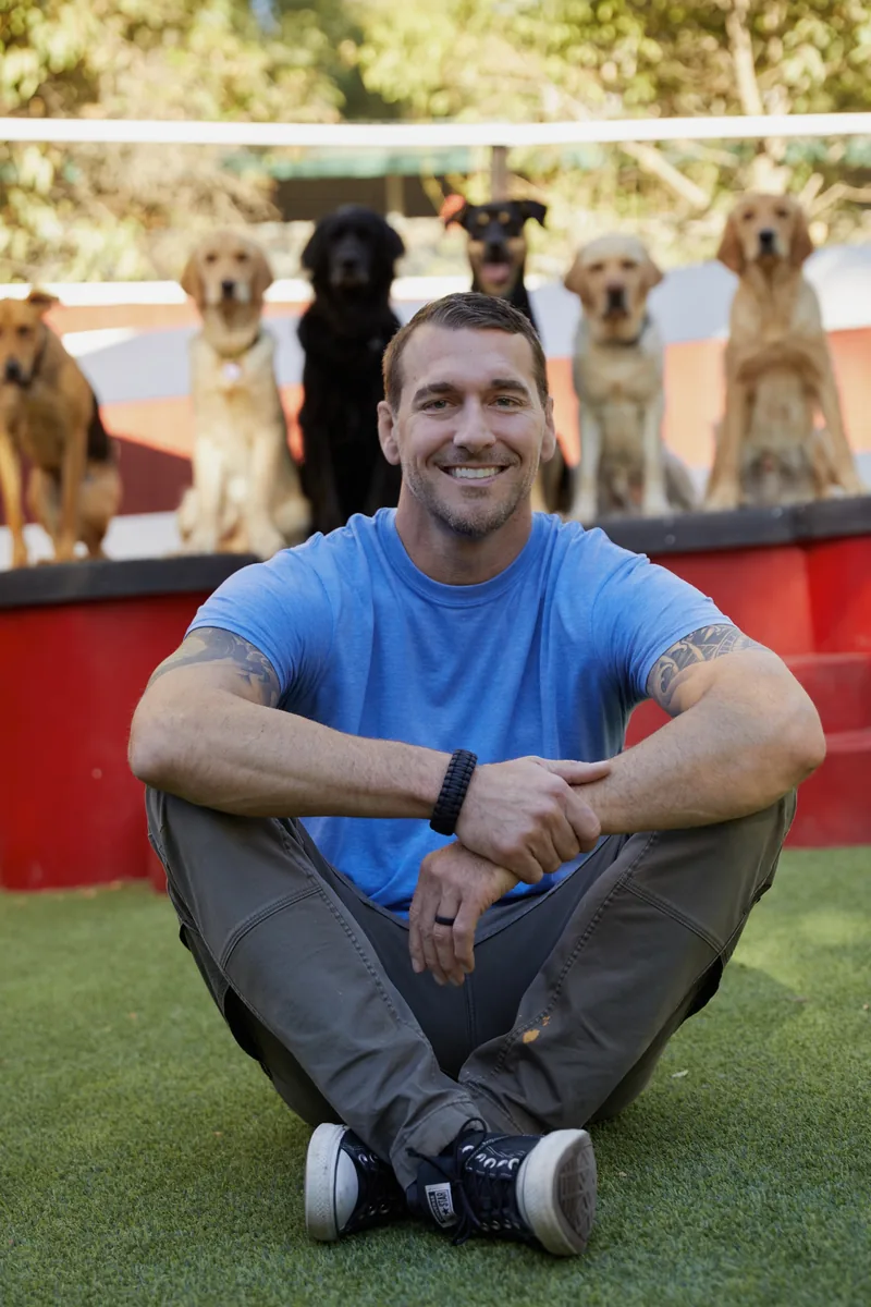 Brandon McMillan sitting on the grass in front of a row of dogs
