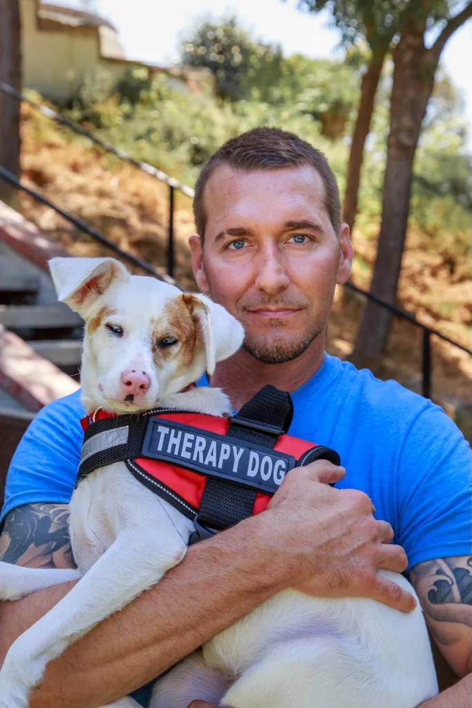 Brandon McMillan holding a puppy wearing a therapy dog vest